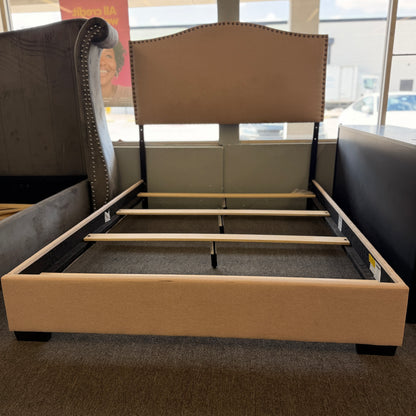 A low-profile queen platform bed frame with a fabric upholstered camelback headboard featuring brass nailhead trim.