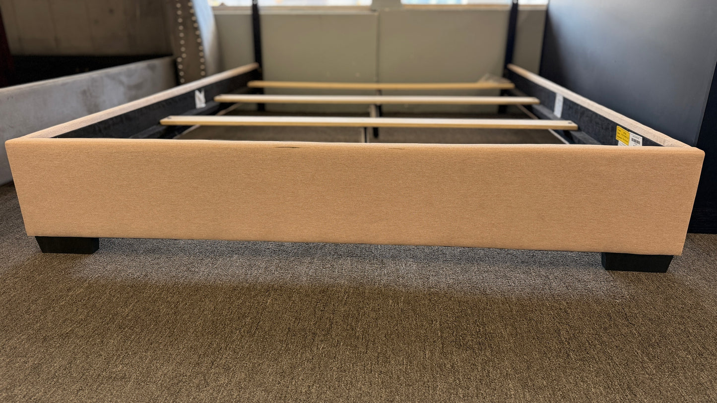 A low-profile queen platform bed frame with a fabric upholstered camelback headboard featuring brass nailhead trim.