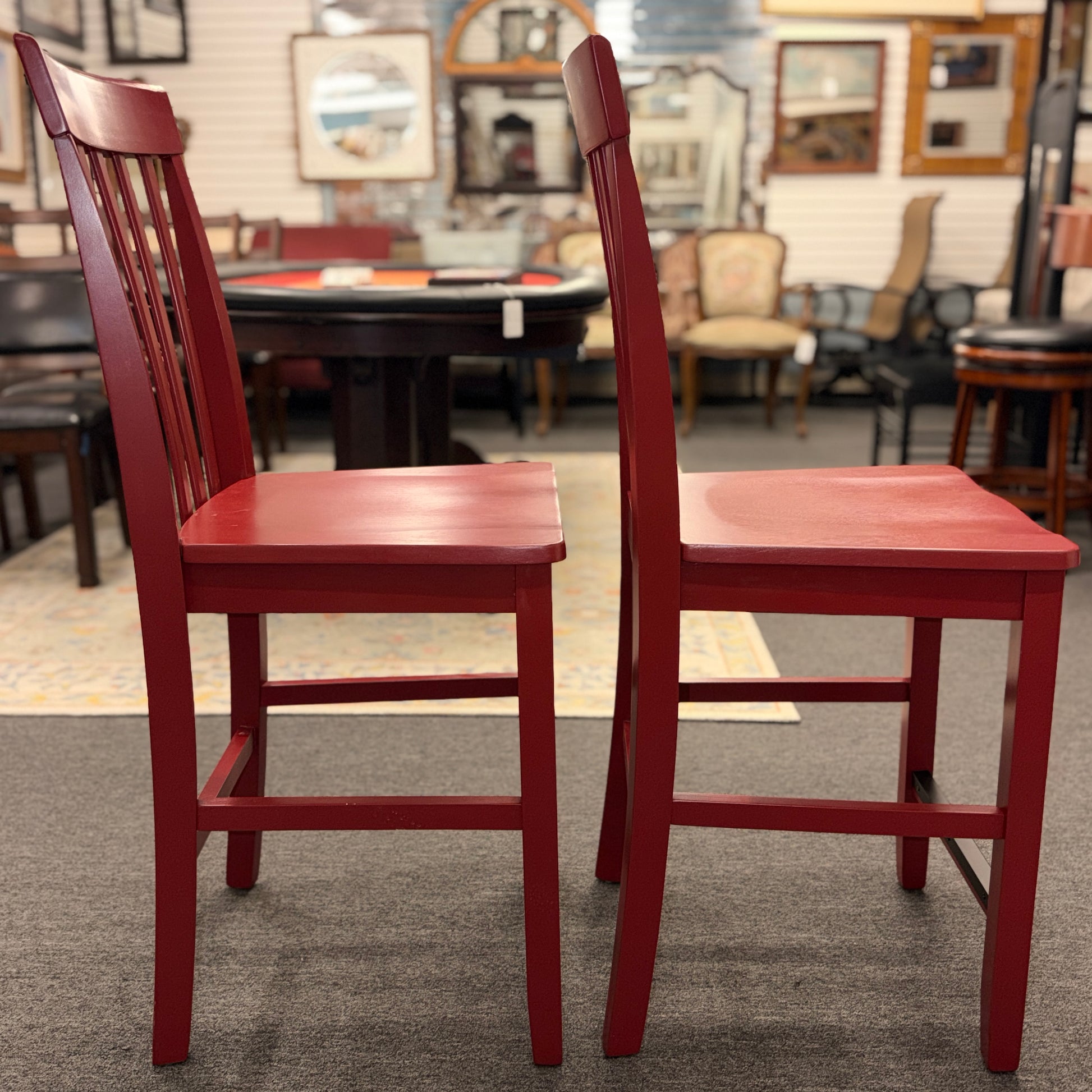 A pair of bright red wooden counter-height barstools featuring vertical slatted backrests, contoured seats, and contrasting black footrest bars.