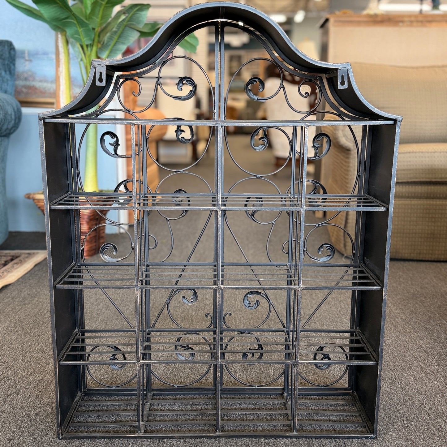 A decorative wall-mounted metal cabinet featuring an arched top, multi-tier interior shelves, and two intricate scrollwork doors that latch in the center.