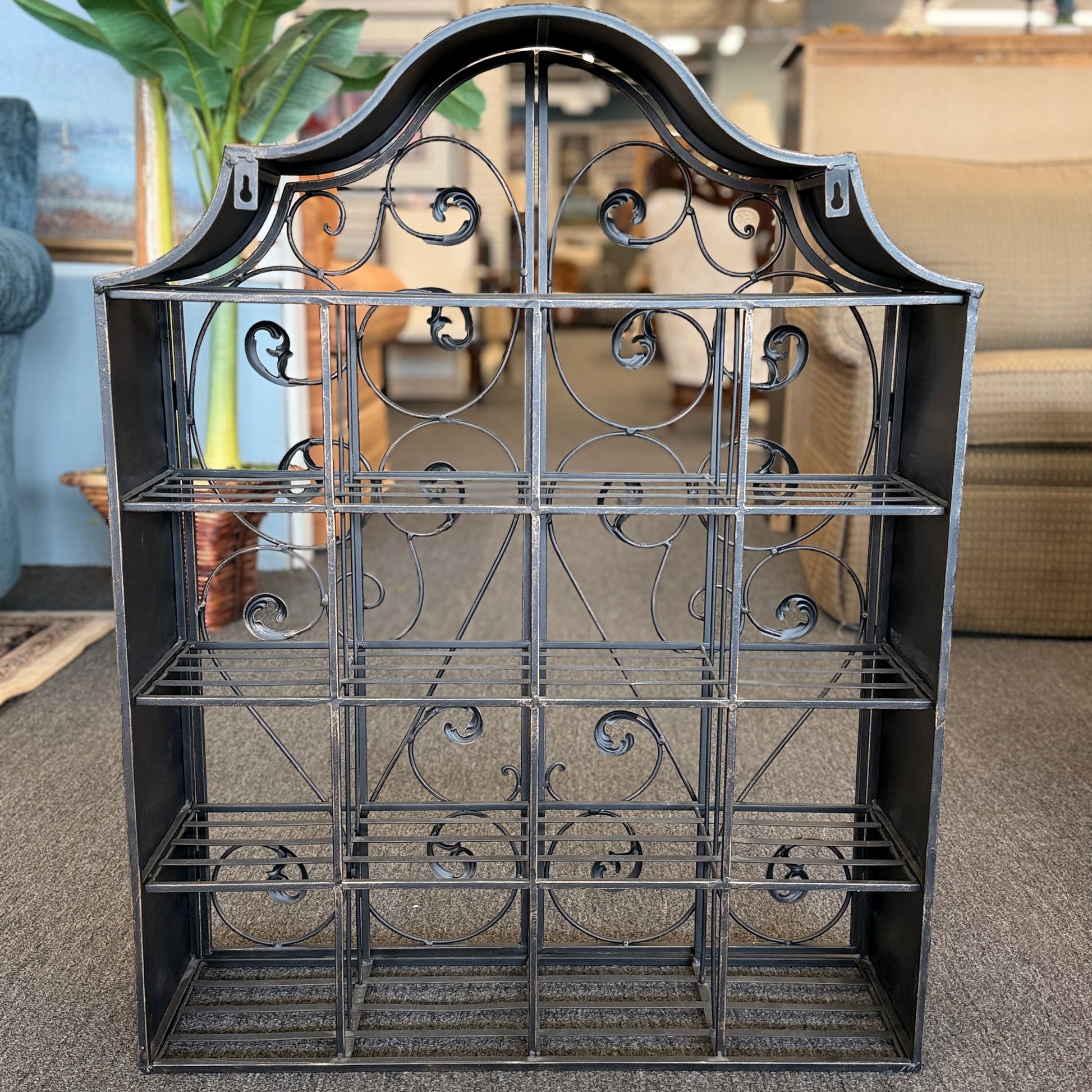 A decorative wall-mounted metal cabinet featuring an arched top, multi-tier interior shelves, and two intricate scrollwork doors that latch in the center.