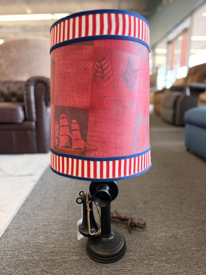 A vintage-style novelty table lamp crafted from a black candlestick telephone base with a red nautical drum shade in good condition.