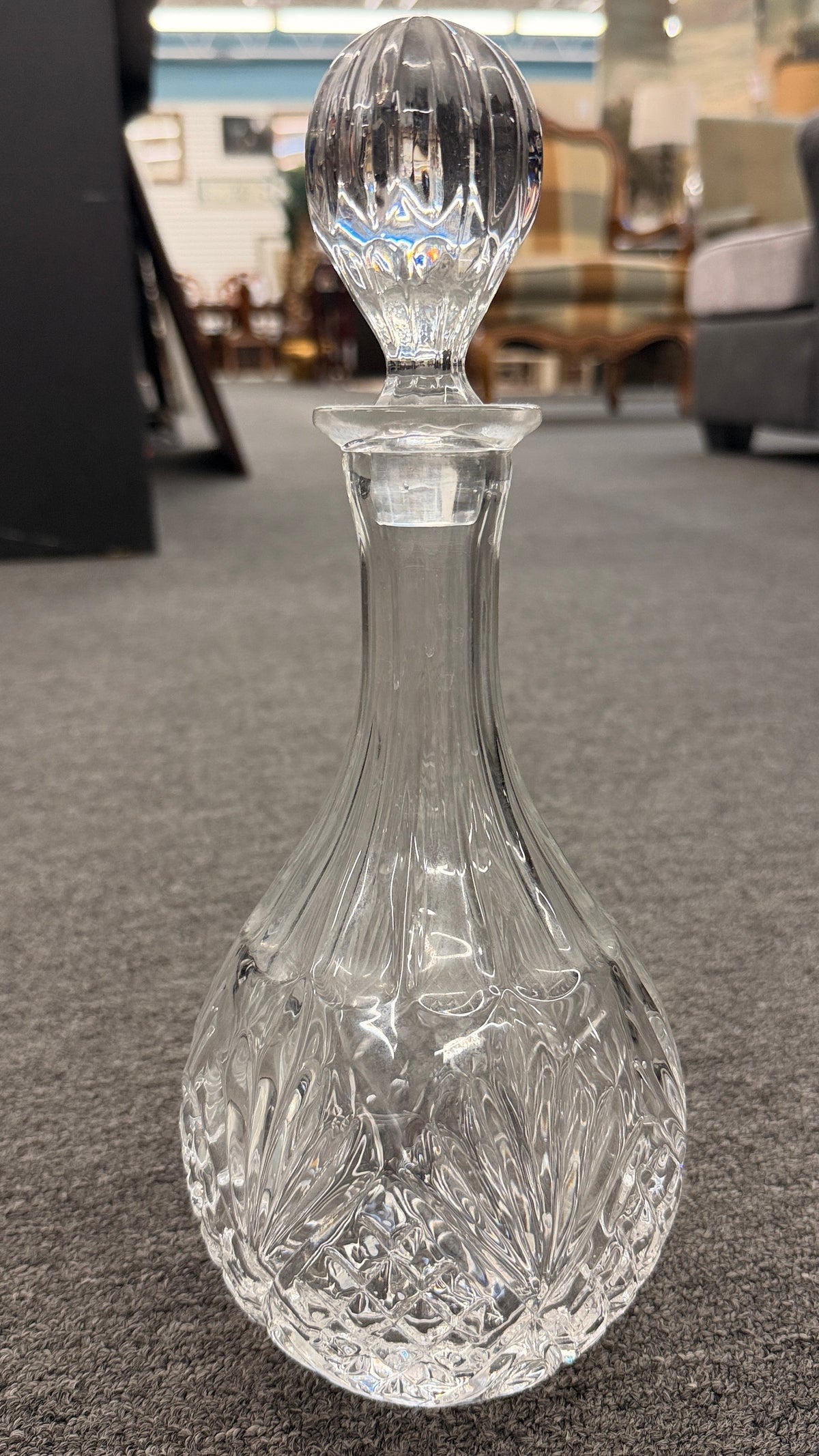 A vintage-style cut-glass decanter with crosshatch and leaf cut patterns, a tall fluted neck, and a matching faceted stopper in excellent condition.
