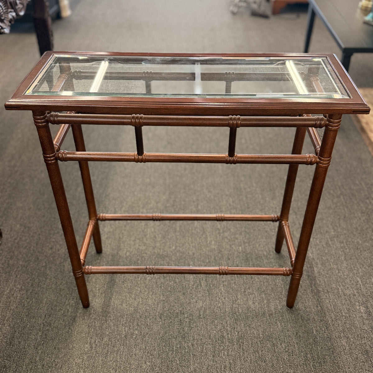 A vintage console sofa table featuring a clear glass top insert set in a faux-bamboo carved wood frame with turned stretchers in good condition.