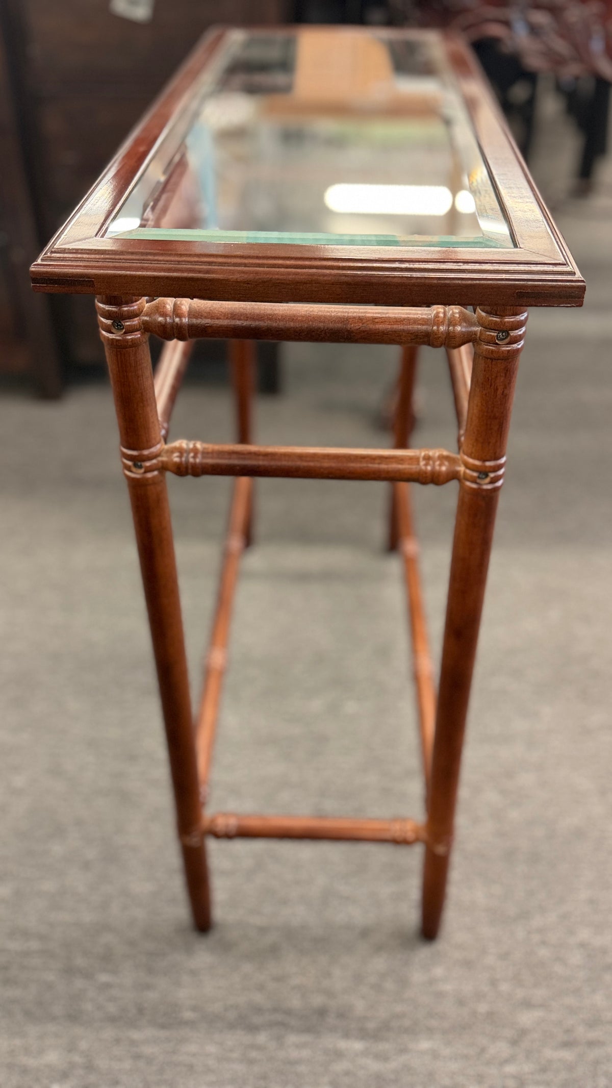 A vintage console sofa table featuring a clear glass top insert set in a faux-bamboo carved wood frame with turned stretchers in good condition.