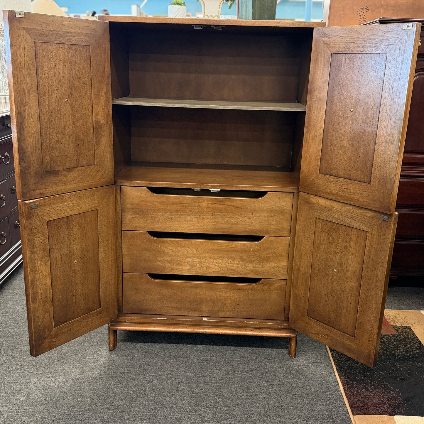 A vintage wooden armoire storage cabinet featuring a symmetric four-panel door facade with recessed molding and antiqued brass ring pull handles.