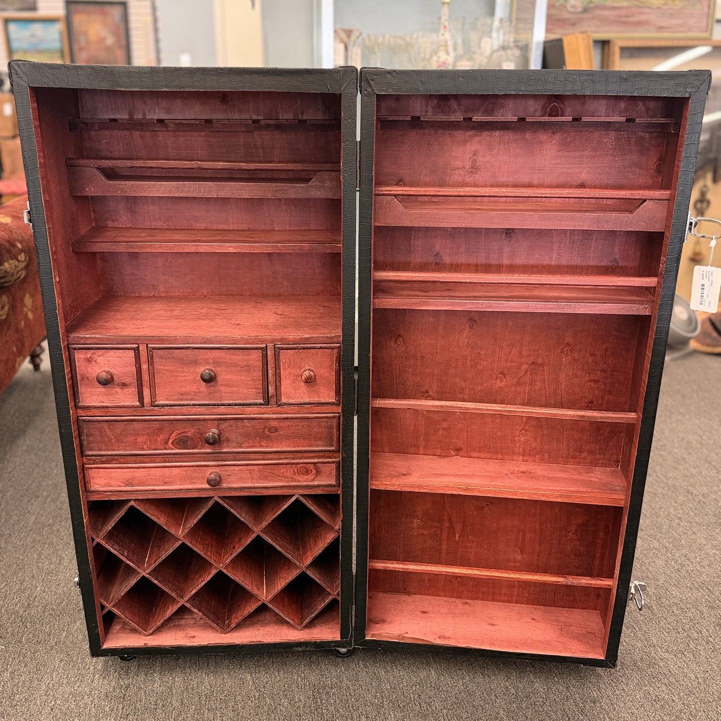 A tall hinged trunk-style bar cabinet featuring interior shelving, small utility drawers, and a lower lattice rack for wine bottle storage.