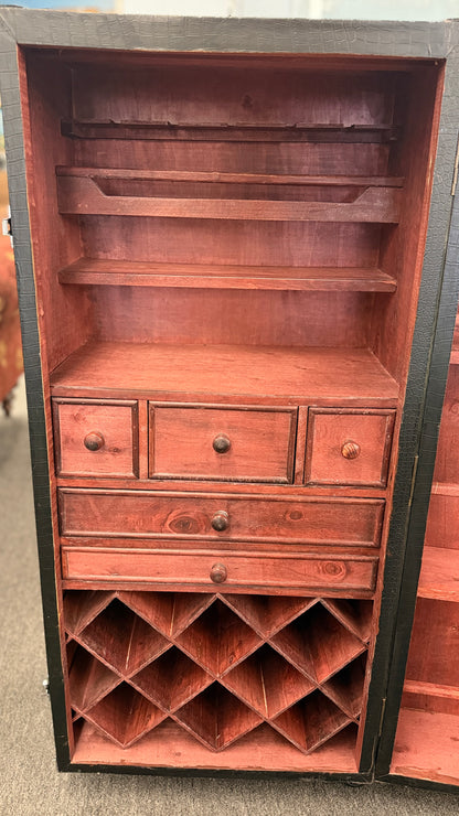 A tall hinged trunk-style bar cabinet featuring interior shelving, small utility drawers, and a lower lattice rack for wine bottle storage.