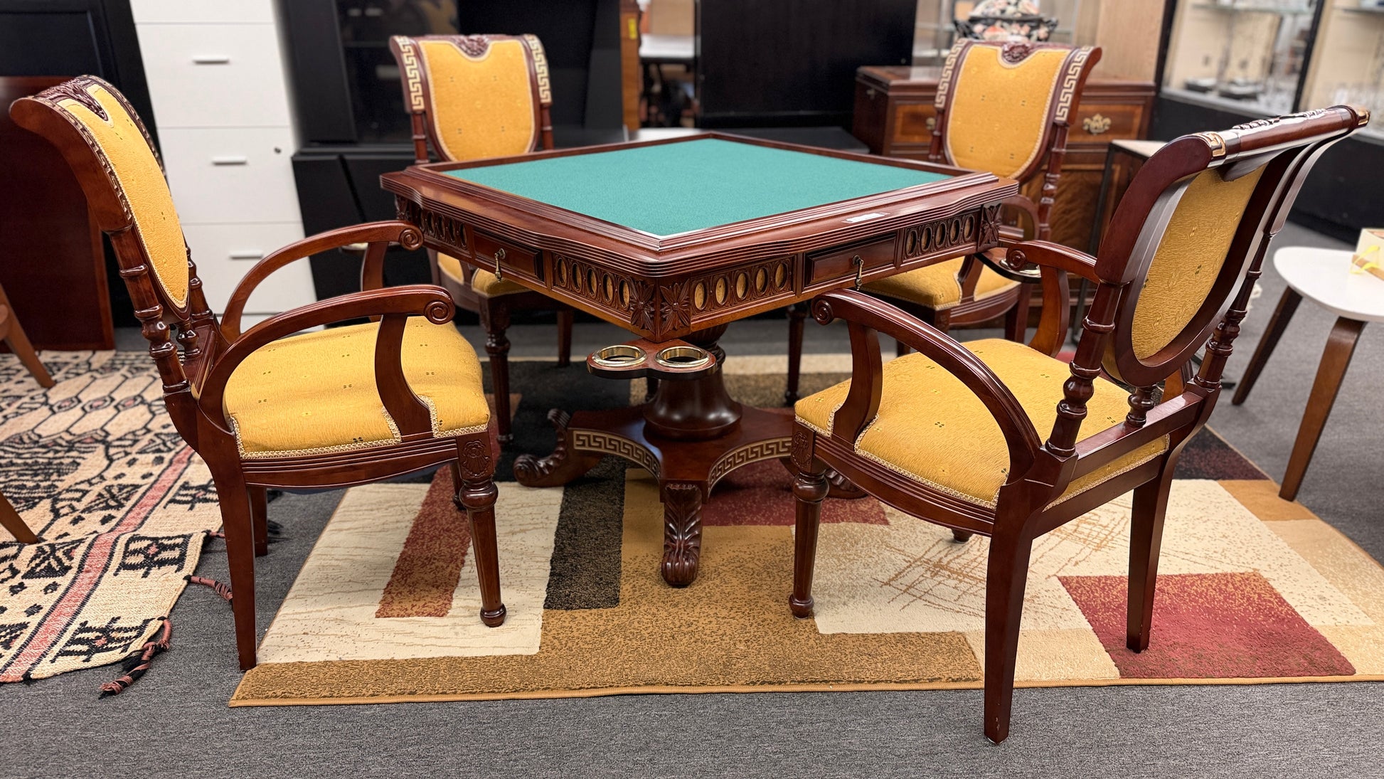 A 5-piece traditional game table set featuring a square wood table with a green felt surface and cup holders, surrounded by four rolling armchairs in yellow patterned upholstery with a Greek key trim.