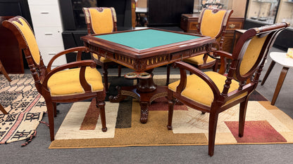 A 5-piece traditional game table set featuring a square wood table with a green felt surface and cup holders, surrounded by four rolling armchairs in yellow patterned upholstery with a Greek key trim.