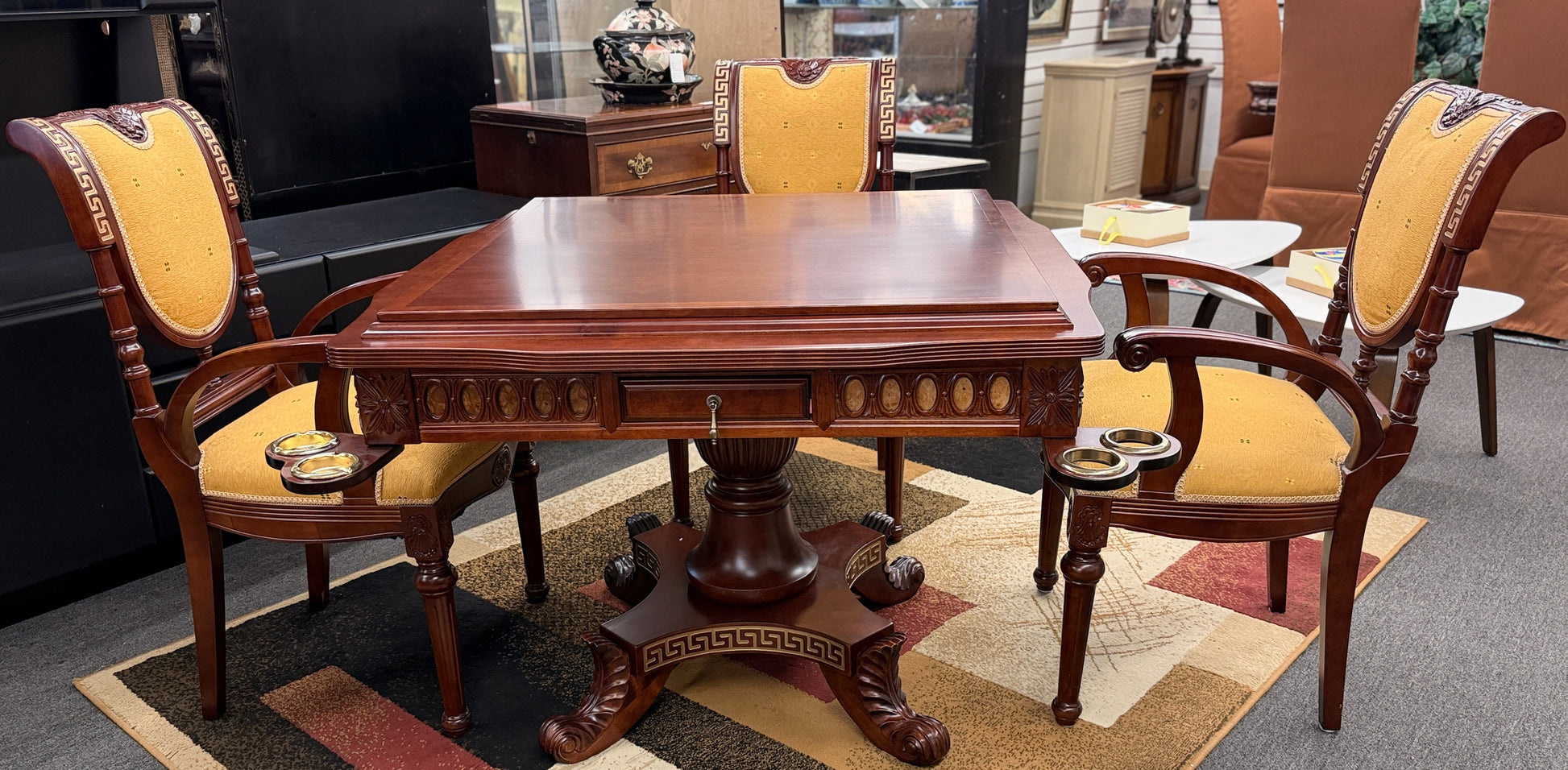 A 5-piece traditional game table set featuring a square wood table with a green felt surface and cup holders, surrounded by four rolling armchairs in yellow patterned upholstery with a Greek key trim.
