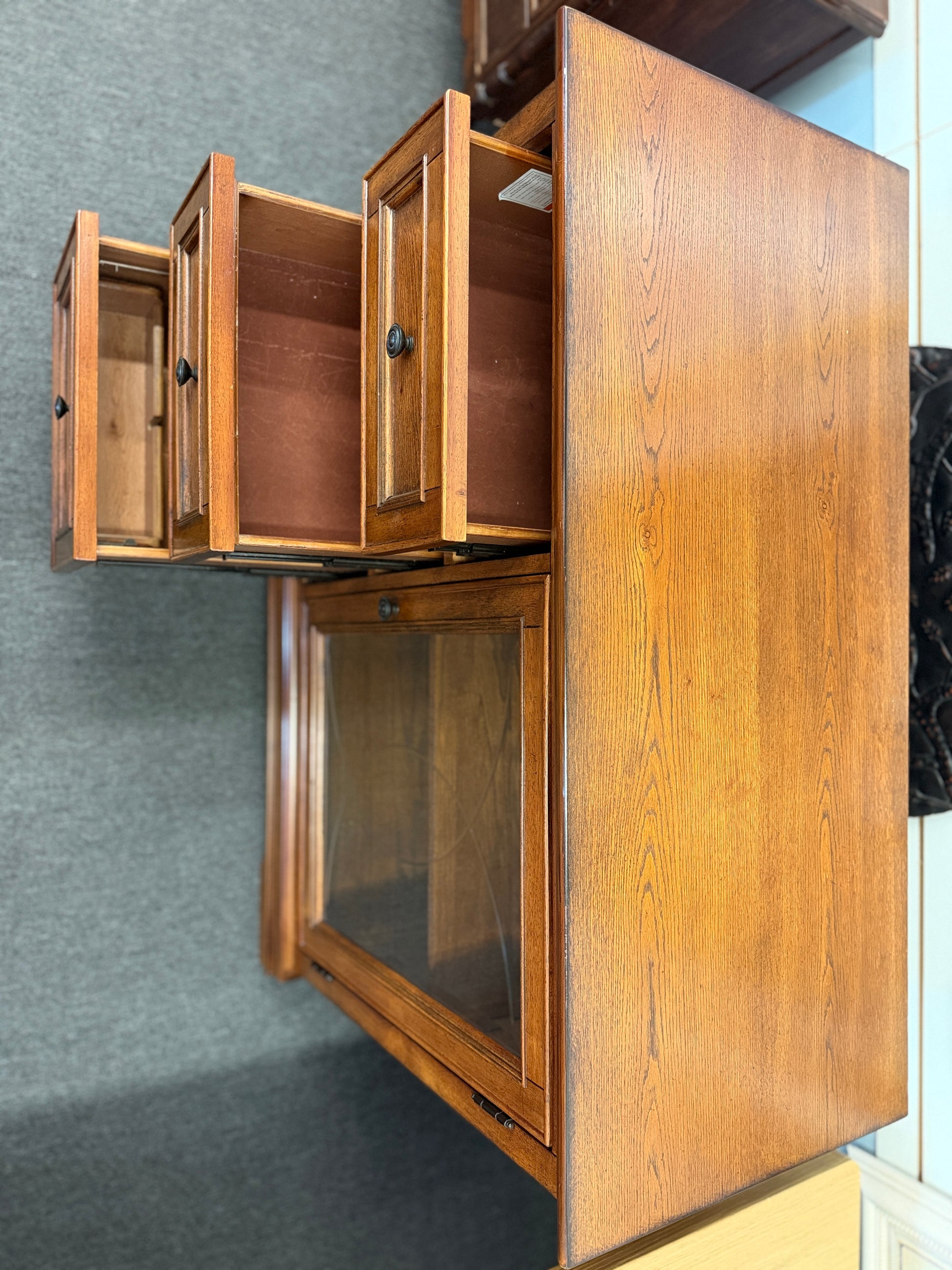 Medium-tone wood storage cabinet featuring three stacked drawers, a glass-paneled cabinet door with interior shelving, and a classic versatile design.