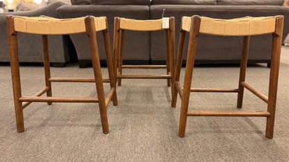 A set of three wooden backless barstools featuring woven natural-fiber seats in good condition.