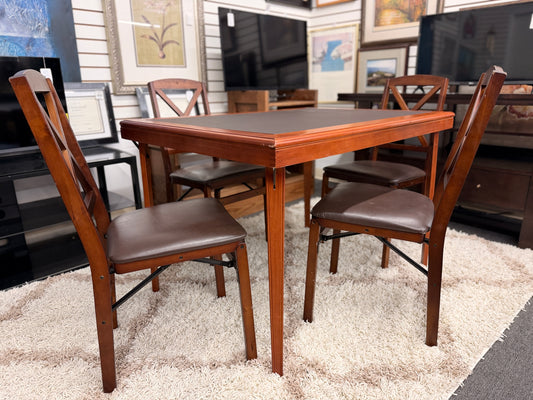 A wooden folding dining table set featuring a dark brown inset playing surface and four matching folding chairs with dark brown upholstered seat cushions.