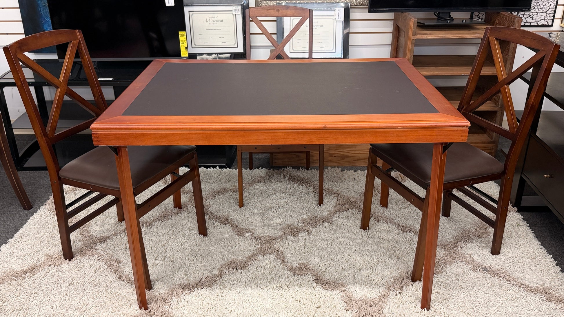 A wooden folding dining table set featuring a dark brown inset playing surface and four matching folding chairs with dark brown upholstered seat cushions.