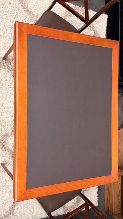 A wooden folding dining table set featuring a dark brown inset playing surface and four matching folding chairs with dark brown upholstered seat cushions.