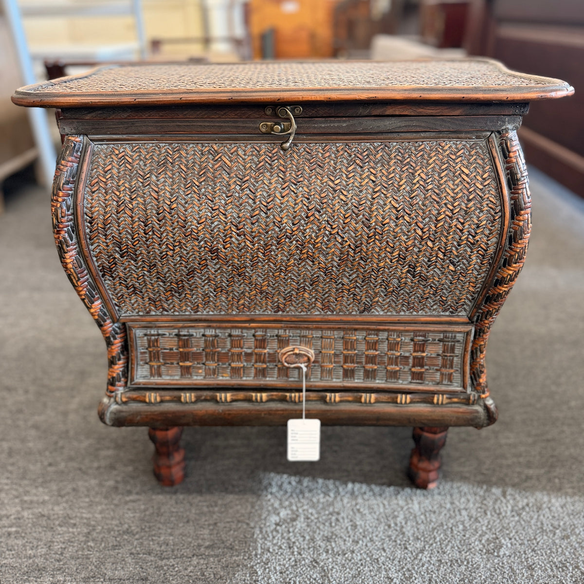A woven rattan storage chest with a latching lid, a textured front panel, and short wooden legs in good condition.