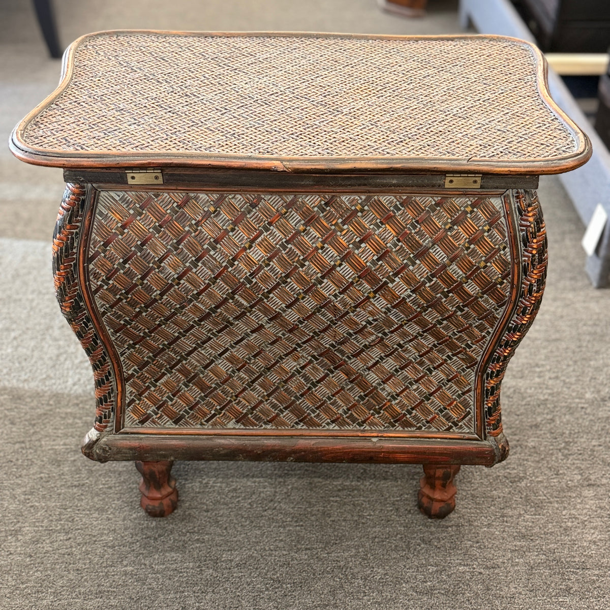 A woven rattan storage chest with a latching lid, a textured front panel, and short wooden legs in good condition.