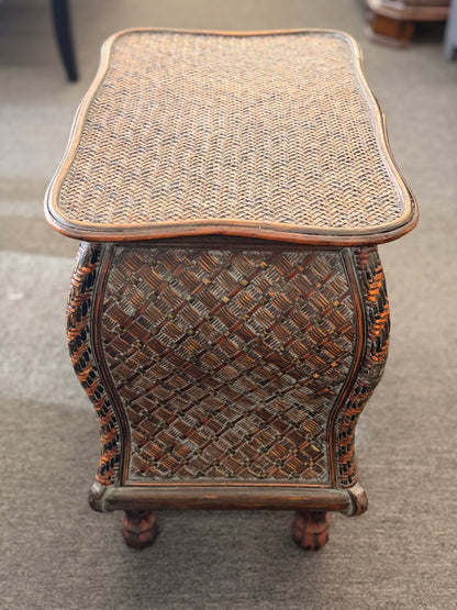 A woven rattan storage chest with a latching lid, a textured front panel, and short wooden legs in good condition.