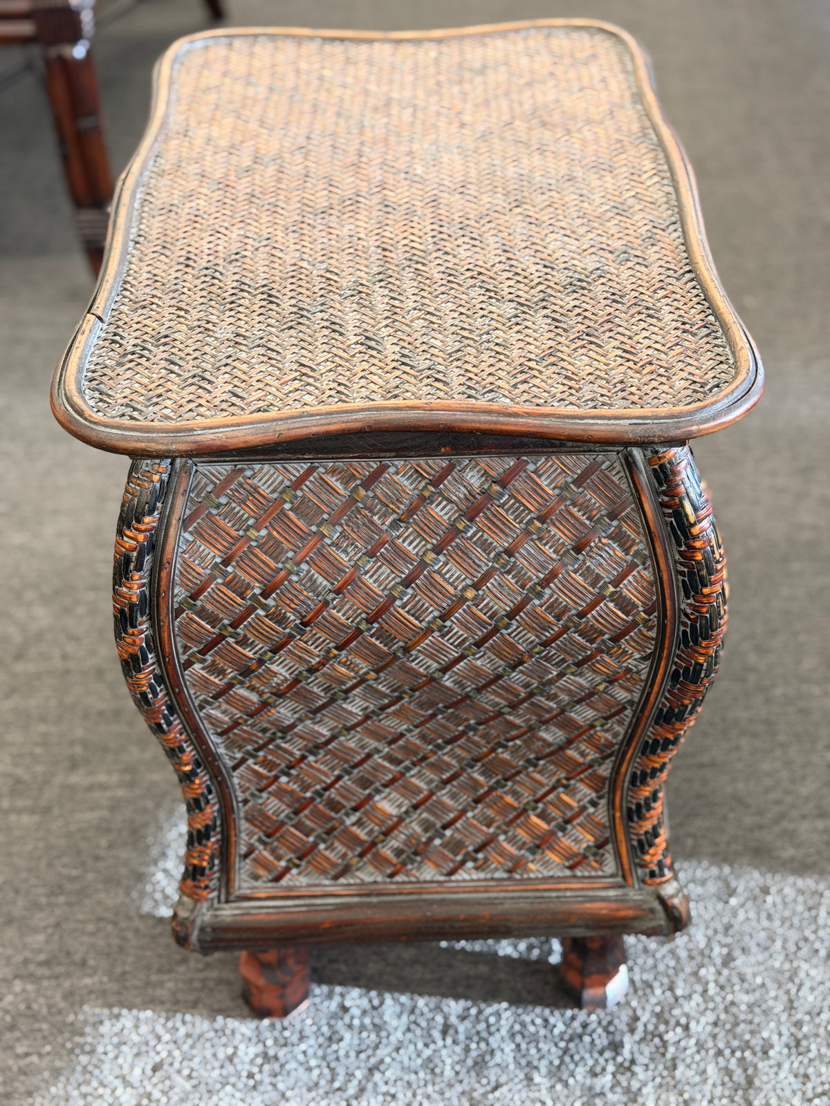 A woven rattan storage chest with a latching lid, a textured front panel, and short wooden legs in good condition.