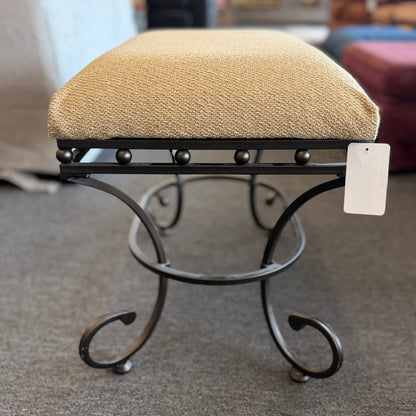 A wrought-iron vanity bench featuring scrollwork legs, studded metal apron trim, and a textured beige tweed upholstered cushion in excellent condition.