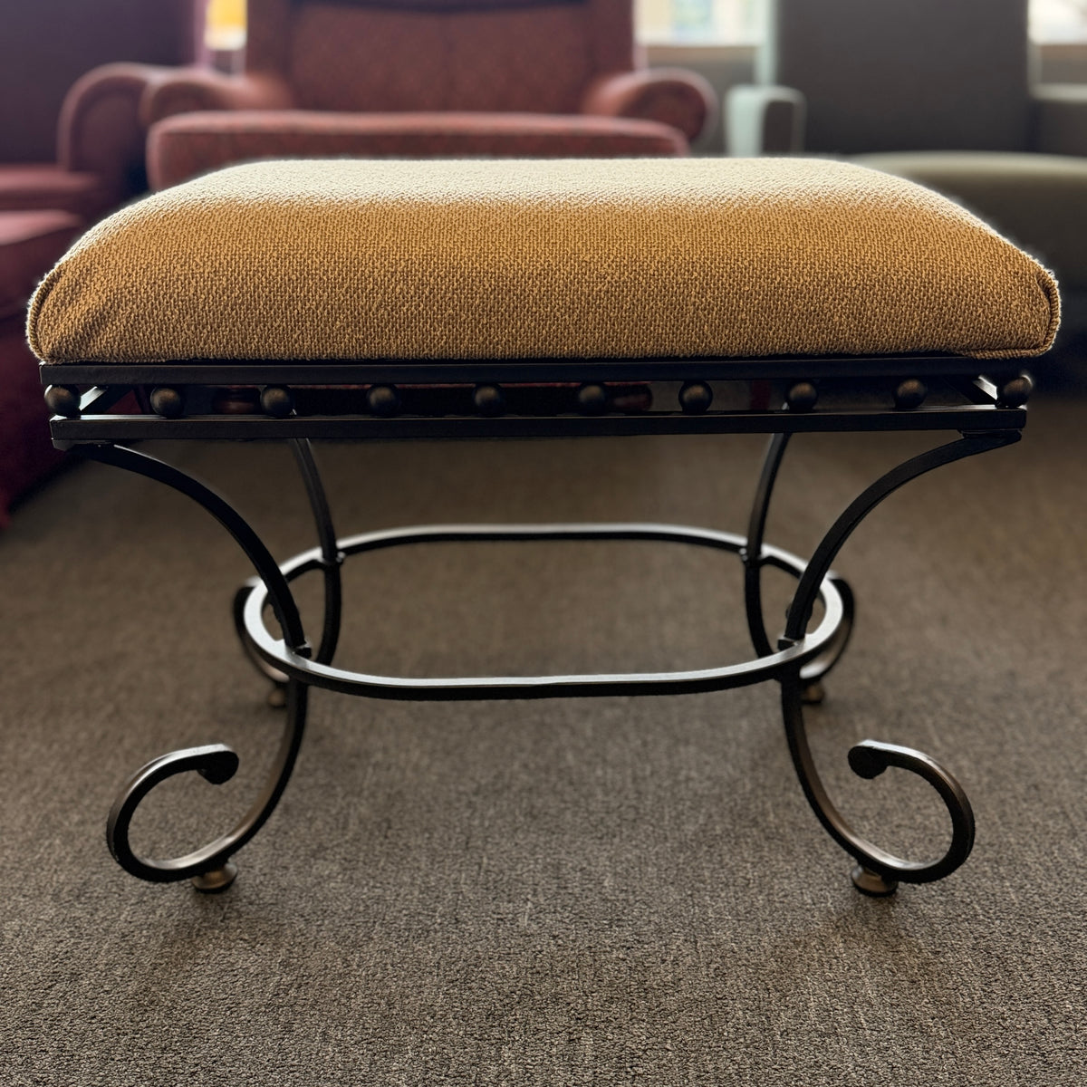 A wrought-iron vanity bench featuring scrollwork legs, studded metal apron trim, and a textured beige tweed upholstered cushion in excellent condition.